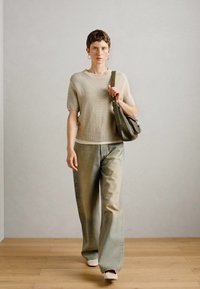 Pull en laine beige à manches courtes, pantalon en denim vert clair ample et sac en bandoulière vert foncé. Des chaussures blanches plates complètent le look.