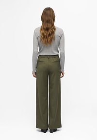 Šedý dlouhý rukáv s ribbovanou strukturou v kombinaci s kalhotami s vysokým pasem v olivově zelené barvě s širokými nohavicemi a dvěma zadními kapsami.