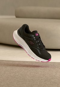 Chaussure de sport noire avec tige en maille et accents roses. Dispose d'une semelle intermédiaire blanche et d'une semelle extérieure texturée. Logo sur le côté et la languette.