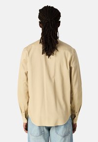 Camicia beige a maniche lunghe con vestibilità rilassata, polsini abbottonati e orlo curvo. Tessuto dal tocco morbido e design semplice.