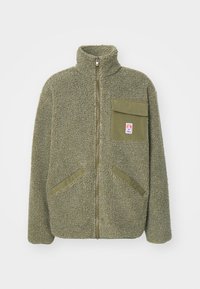 Giacca in pile verde oliva, caratterizzata da un alto colletto, zip frontale, una tasca sul petto e due tasche laterali diagonali. Superficie testurizzata.