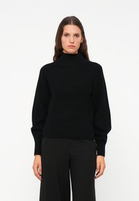 Schwarzer gerippter Rollkragenpullover mit lockerer Passform, langen �Ärmeln und strukturierten Oberfläche. Kombiniert mit schwarzen weit geschnittenen Hosen.