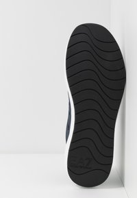 Schwarze Gummisohle mit strukturiertem Muster; erhabene Rillen bieten Halt. Enthält einen weißen Rand und geprägtes EA7-Logo zur Markenidentifikation.