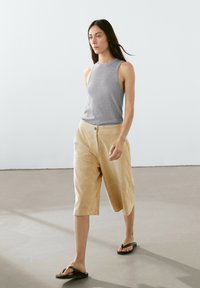 Grijze mouwloze top, beige wijde shorts met knoopsluiting en zwarte slippers. Glad materiaal met een ontspannen pasvorm; minimalistisch ontwerp.