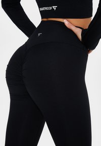 Black fitness leggings with a high waistband, ruched detail at the back, and soft, stretchy fabric. The design features a visible logo.