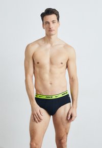 Schwarze Slips mit einem neongrünen Bund, der das Nike-Logo trägt. Sie bestehen aus einem glatten Stoff, haben eine figurbetonte Passform und einen niedrigen Schnitt.