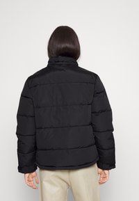 Giubbotto a vento nero con colletto alto, design trapuntato e polsini a coste. Presenta una texture liscia e una vestibilità comoda, visto da dietro.