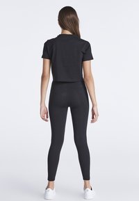 Černé cropped tričko spárované s černými legínami. Tričko má krátké rukávy a kulatý výstřih. Hladká, elastická látka. Bílé tenisky.