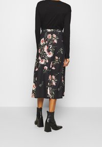 Černá midi sukně s květinovým vzorem v růžových a zelených barvách, kombinovaná s černými kotníkovými botami a černým topem s dlouhým rukávem.