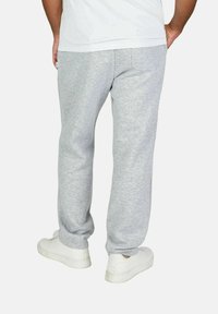 Graue, lässige Baumwollsweatpants mit entspanntem Schnitt, glatter Textur, elastischem Bund und Seitentaschen. Getragen mit weißen Sneakers.