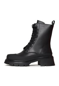 Botas negras de cuero hasta el tobillo con un diseño de cordones, suela de plataforma gruesa y taco estriado. Cuenta con una pestaña en la parte posterior para facilitar el calzado.