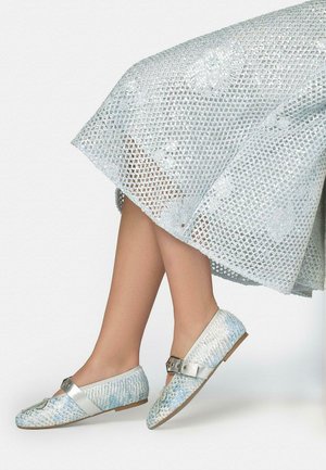 Picioare îmbrăcate într-o fustă texturată albastru deschis și pantofi comozi asortați, cu baretă și decorațiuni florale, pe un fundal alb.