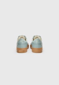 Light blue leather sneakers with a tan rubber sole, rounded toe, and brand detailing on the back. Smooth texture with gold accents.