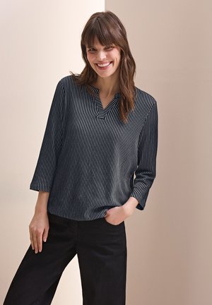 Blouse rayée en bleu marine et blanc, avec un col en V et des manches trois-quarts. Tissu doux avec une coupe décontractée, associée à un pantalon noir.