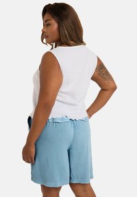 White sleeveless top with a scalloped hem, paired with light blue shorts featuring a loose fit and back pockets. Soft, textured fabric.