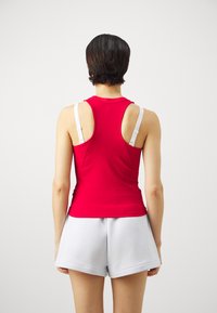 Rotes geripptes Tanktop mit weißen Trägern, figurbetontem Design und rundem Ausschnitt. Kombiniert mit hellgrauen Shorts, die einen lässigen Stil präsentieren.