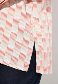 Camicia a maniche corte in tessuto leggero con un motivo geometrico di strisce corallo e crema, con una spacco laterale e una vestibilità rilassata.