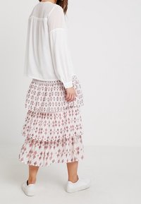 Blusa bianca a maniche lunghe con yoke testurizzato abbinata a una gonna maxi a strati con motivo a diamante bianco e rosso. Sneakers bianche completano il look.