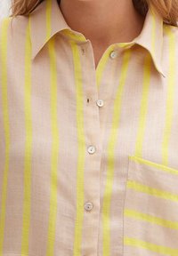 Light beige shirt featuring bright yellow vertical stripes, a collar, button-down front, and a chest pocket. Buttons are white and round.