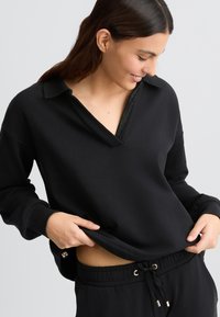 Sweatshirt noir à col polo avec un détail texturé en V. Tissu doux, coupe décontractée et manches longues.