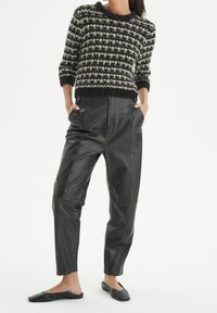 Pull en tricot avec un motif à carreaux noir et crème ; associé à un pantalon en cuir noir taille haute ; le modèle porte des chaussures noires à enfiler.
