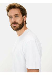 Hvid kortærmet t-shirt lavet af letvægtigt stof, med rund halsudskæring og en afslappet pasform, samt synlige syninger.