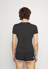 Camiseta deportiva negra de manga corta, con forma ajustada, detalle de costura visible, combinada con pantalones cortos negros que tienen acentos blancos.