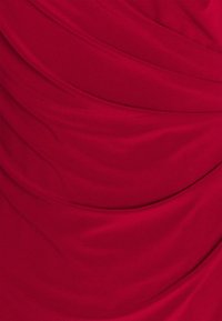 Tela roja drapeada con una textura suave, mostrando pliegues y costuras fluidas y suaves, creando una apariencia en capas en la superficie.