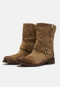 Botas de tobillo de ante marrón con un patrón texturizado, tacón plano y detalle de correa con hebilla. Punta redondeada y acentos cosidos en la parte superior.