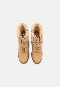 Tan ankle boots with faux fur lining, lace-up design, and side zipper. Soft suede texture with rubber soles and gold-tone hardware accents.