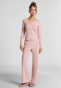 Lichtroze geribd topje met een V-hals en knoopdetails, gecombineerd met bijpassende uitlopende broek. Zachte stoftextuur en een comfortabele pasvorm.