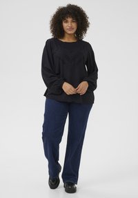 Black blouse with intricate stitched design, loose fit, and long sleeves, paired with dark blue wide-leg jeans and black shoes.