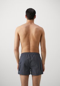 Costumi da bagno da uomo grigio scuro con vita elastica, due tasche laterali e design casual, realizzati in un materiale leggero e con un taglio short.