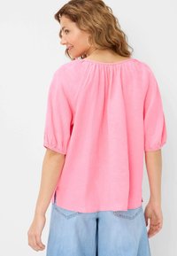 Top in lino rosa con una vestibilità morbida, maniche corte a palloncino e yoke sul retro arricciato. Le fessure laterali e la texture leggera aumentano il comfort.