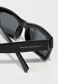Ochelari de soare negri cu lentile gri, ramă largă și finisaj lucios. Prezintă logo-ul 'PRIVÉ REVAUX' pe timpă. Formă rectangulară clasică.