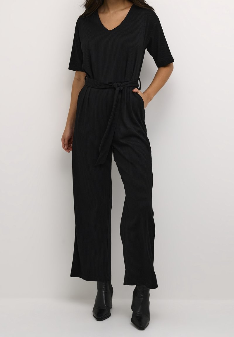 Jumpsuit negro acanalado con escote en V, mangas cortas, cintura ceñida por un cinturón, diseño de pierna ancha y bolsillos en las costuras. LlevaBotines.
