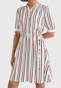 Vit kortärmad klänning med vertikala ränder i röd och marinblå med cirkulära mönster, knäppning fram och justerbar midja.