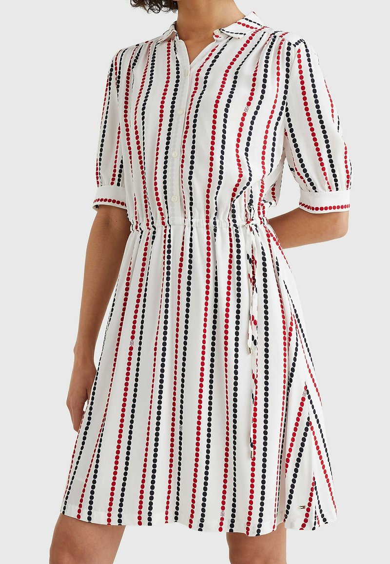 Vit kortärmad klänning med vertikala ränder i röd och marinblå med cirkulära mönster, knäppning fram och justerbar midja.
