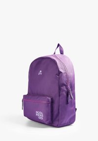 Mochila morada hecha de un tejido duradero, con una forma curveada, bolsillo frontal con cremallera, detalle del logo y un asa en la parte superior para llevarla.