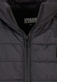 Crna podstavljena jakna s patentnim zatvaračem sprijeda, kviltanom teksturom i pričvršćenim kapuljačom. Sadrži oznaku "URBAN CLASSICS" unutra. Veličina srednja.
