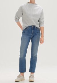 Randig grå tröja med hög krage, kombinerad med blå raka jeans och ljusa sneakers. Texturen verkar mjuk och avslappnad.