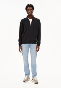 Dunkelblauer Quarter-Zip-Pullover aus Baumwollmischung mit flachem Kragen. Hellblaue gerade Jeans. Kombiniert mit grauen Sneakern.