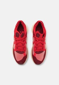 Une paire de chaussures de sport rouges avec des panneaux en maille et en daim, des semelles beiges et des lacets rouges, vue de dessus sur fond blanc.