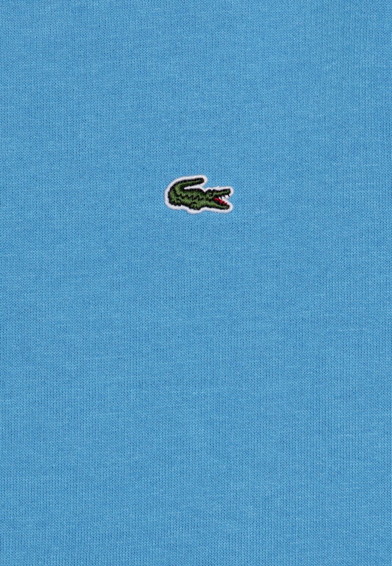 Hellblaues Baumwoll-Polohemd mit einem kleinen grünen Krokodil-Logo, das auf der Brust gestickt ist, und präsentiert eine glatte Textur sowie ein klassisches Design.