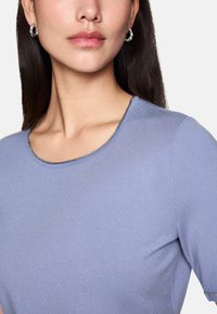 Helles lila kurzärmliges Oberteil mit glatter Textur und Rundhalsausschnitt, akzentuiert durch einen subtilen metallischen Besatz entlang des Kragens.