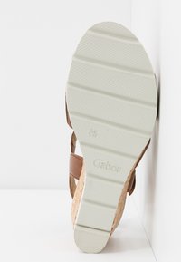 Semelle d'une sandale compensée avec un grip blanc texturé et des côtés tissés marron clair, portant le nom de la marque "Gabor" embossé sur la semelle.