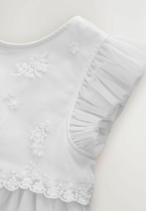 Fehér ruha hímzett virágmintákkal, puha tüll ujjakkal fodrokkal és hullámos csipke szegéllyel az alján.