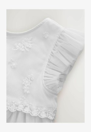 Biała sukienka z wyszywanymi kwiatowymi wzorami, miękkimi rękawami z tiulu z falbankami oraz koronkową lamówką o falistym kształcie na dole.