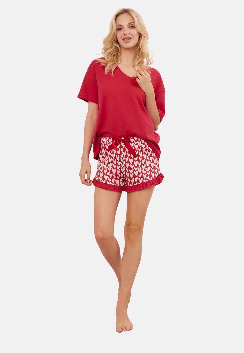 Czerwony top z dekoltem w kształcie litery V w komplecie z czerwonymi szortami z białym wzorem serc i falbaniastym wykończeniem. Miękka tkanina i luźny krój.