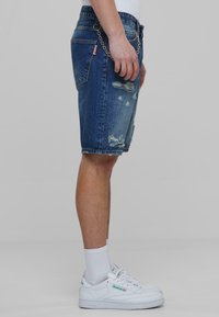 Denim šorti vidēji zilā krāsā, ar nolietotiem akcentiem un saplēstu apakšmalu. Apvienoti ar baltām ikdienas kedām un baltām potīšu zeķēm.